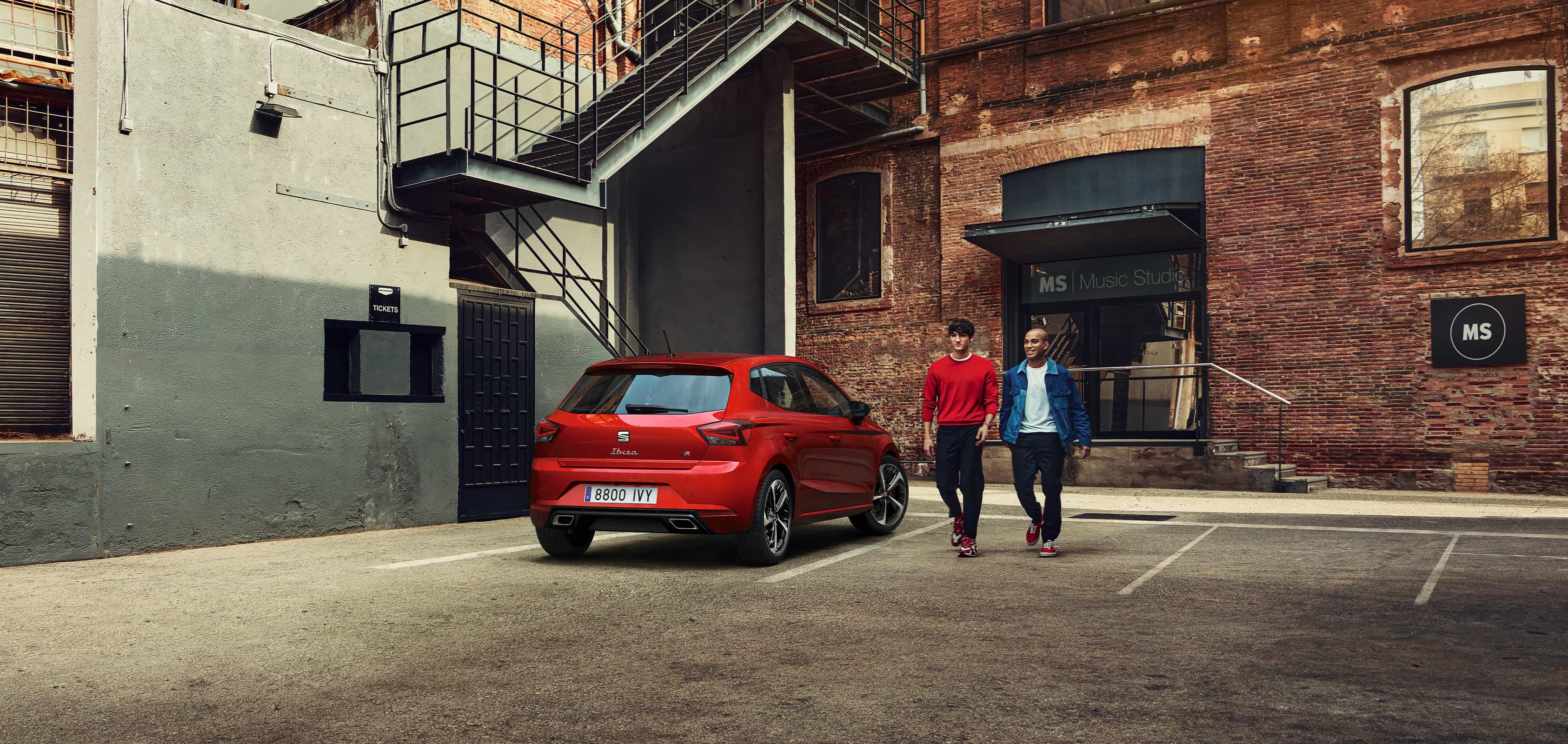 Deux hommes marchent à côté de SEAT Ibiza couleur rouge