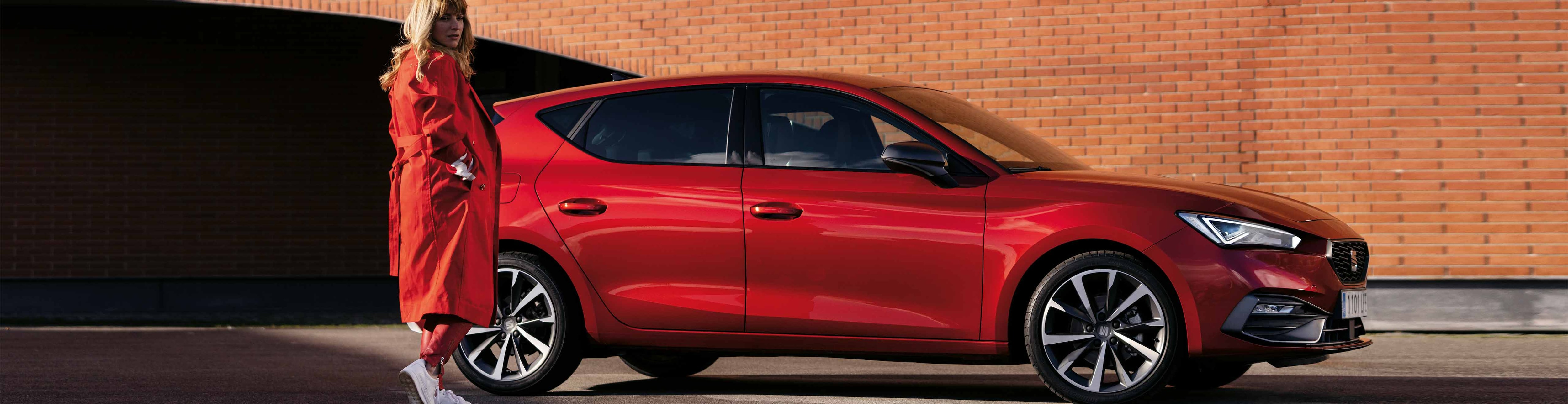 Woman standing next to the SEAT Leon desire red colour with machine alloy wheels